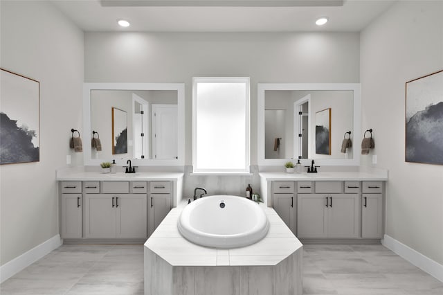 bathroom featuring two vanities, a garden tub, and a sink