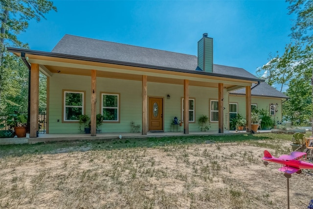 rear view of house featuring a porch, a chimney, and a shingled roof