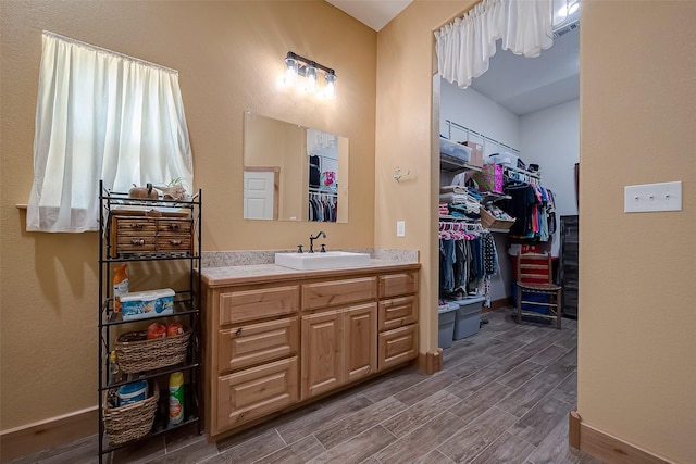 bathroom featuring wood finished floors, visible vents, baseboards, vanity, and a walk in closet