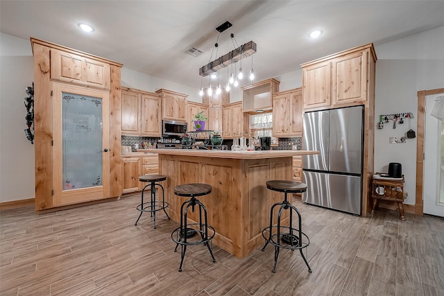 kitchen with visible vents, a breakfast bar, a center island, stainless steel appliances, and light brown cabinets