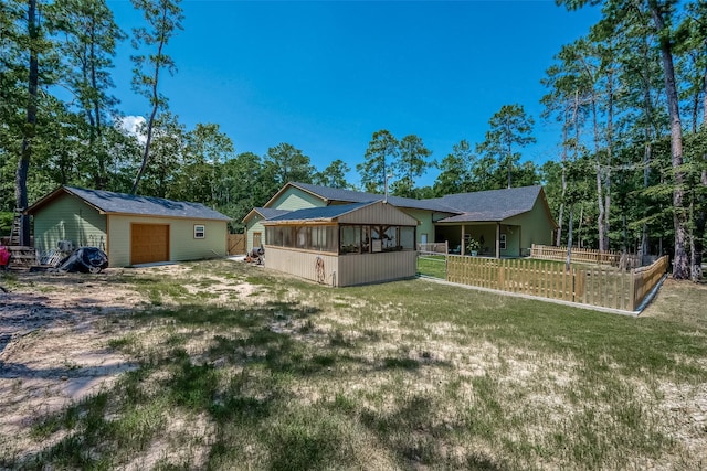 back of property with a yard, a detached garage, fence, and an outdoor structure