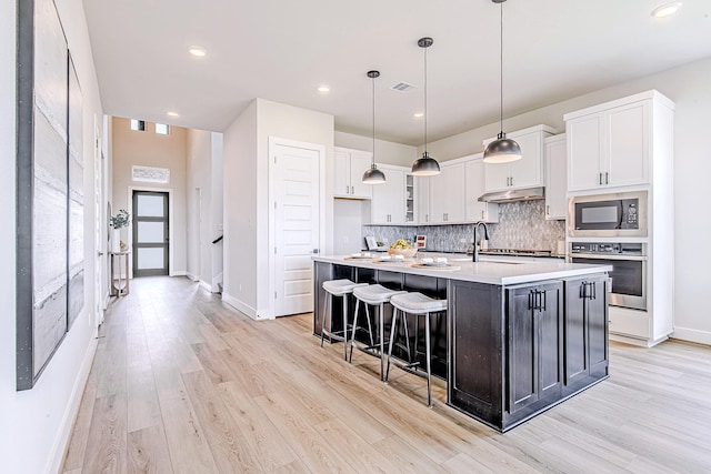 141 Peninsula Point Dr, Montgomery, TX 77356 - kitchen featuring stainless steel oven, black microwave, under cabinet range hood, white cabinets, and backsplash