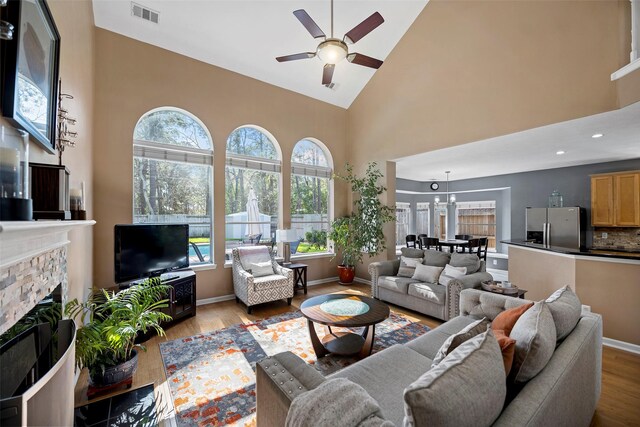 living area with high vaulted ceiling, visible vents, a fireplace, and wood finished floors