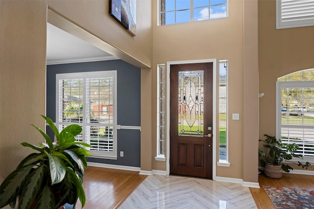entrance foyer with ornamental molding, parquet floors, a towering ceiling, and baseboards