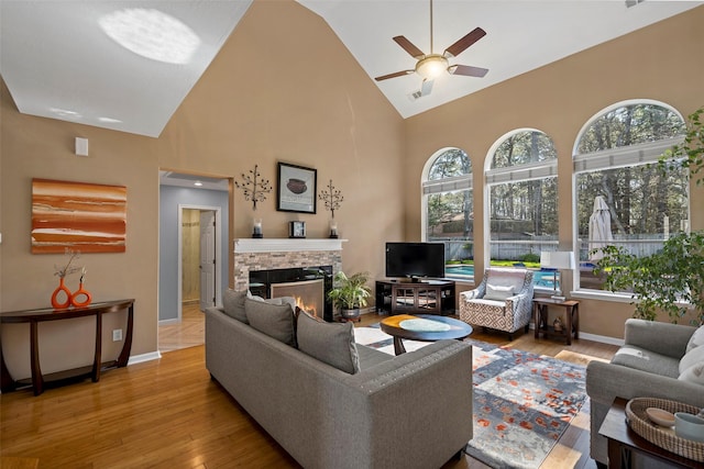 living area featuring baseboards, high vaulted ceiling, wood finished floors, and a stone fireplace