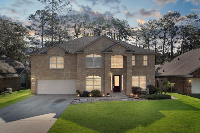 view of front of property featuring an attached garage, brick siding, a shingled roof, a yard, and concrete driveway