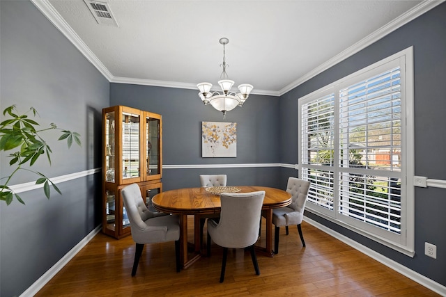 dining area with crown molding, visible vents, an inviting chandelier, wood finished floors, and baseboards