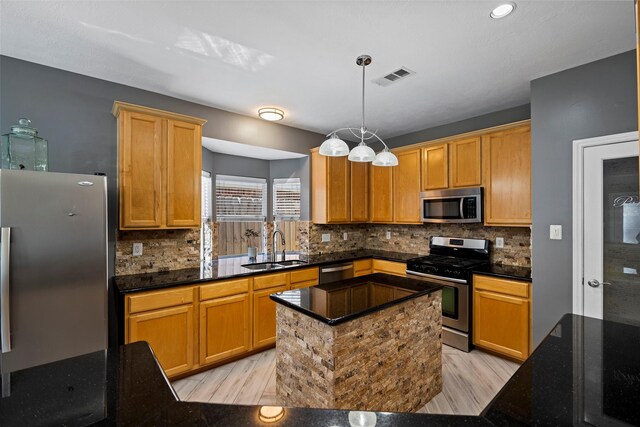 kitchen with a sink, visible vents, appliances with stainless steel finishes, backsplash, and dark stone counters
