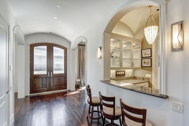 foyer entrance featuring dark wood-style floors, french doors, arched walkways, lofted ceiling, and indoor bar