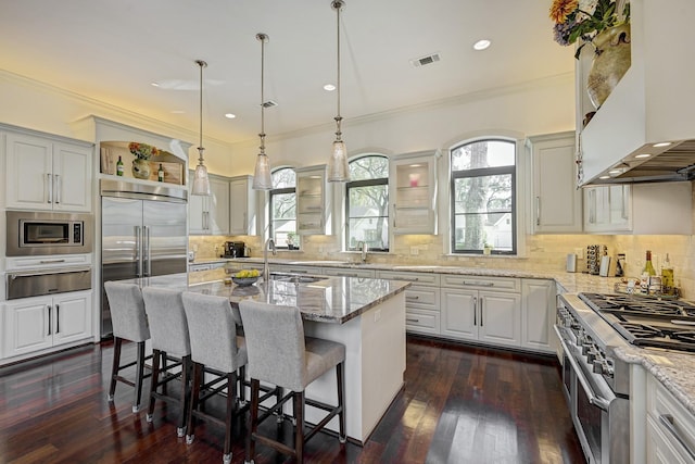 kitchen with range hood, open shelves, a kitchen breakfast bar, built in appliances, and a warming drawer