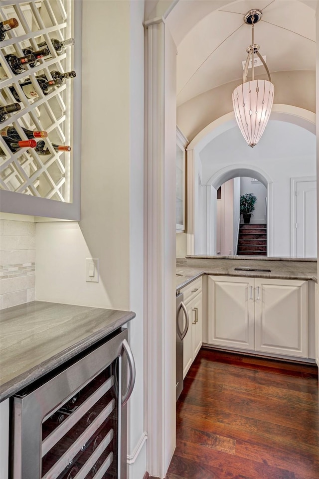 bar with wine cooler, dark wood finished floors, decorative light fixtures, decorative backsplash, and arched walkways