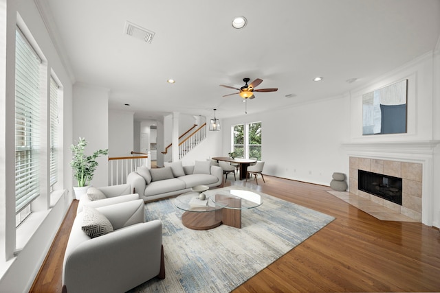 living area featuring stairway, wood finished floors, recessed lighting, a tile fireplace, and crown molding