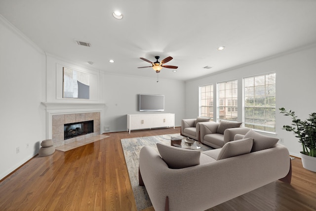 living area with visible vents, wood finished floors, recessed lighting, crown molding, and a tile fireplace