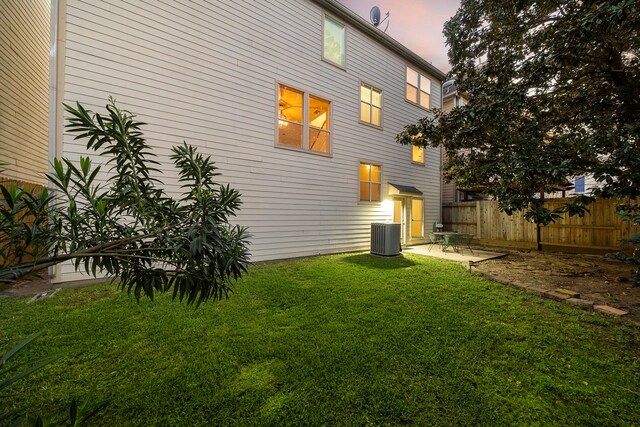 back of property at dusk with a patio area, a yard, central AC, and fence