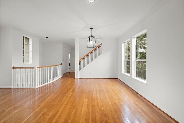 empty room featuring ornate columns, stairway, baseboards, and light wood finished floors