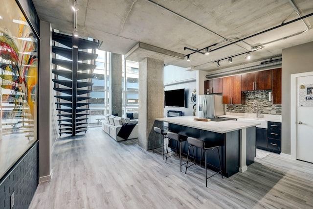 kitchen with light wood-style flooring, a breakfast bar, stainless steel refrigerator with ice dispenser, and decorative backsplash