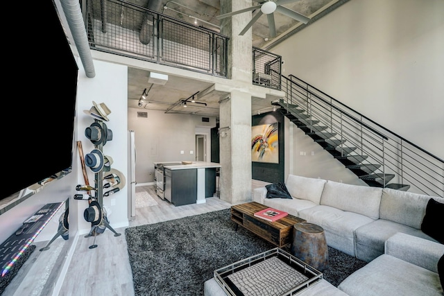 living area featuring a ceiling fan, a towering ceiling, stairway, rail lighting, and light wood-type flooring