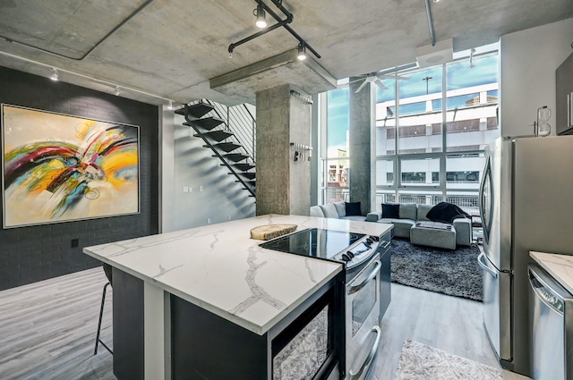 kitchen with light wood-style flooring, a center island, light stone counters, track lighting, and appliances with stainless steel finishes