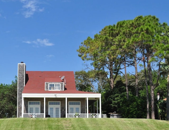 view of front facade with french doors, a chimney, and a front lawn