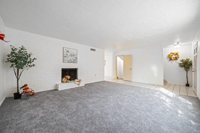 unfurnished living room featuring carpet floors, visible vents, a brick fireplace, a textured ceiling, and tile patterned floors