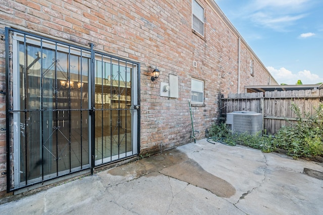 entrance to property featuring central air condition unit, a patio area, fence, and brick siding