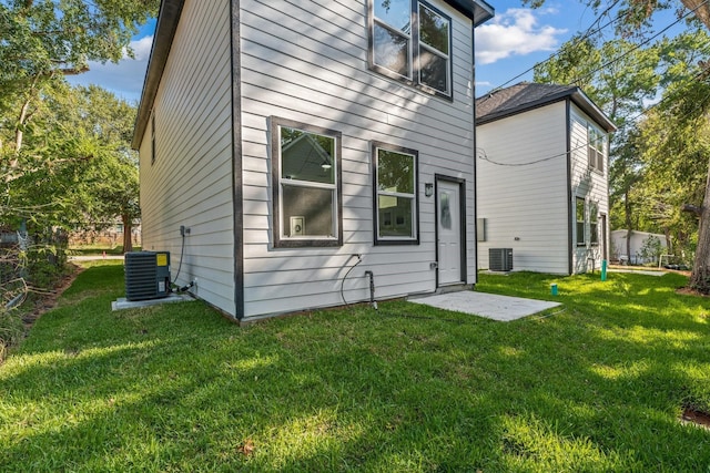 rear view of property with central AC unit and a lawn