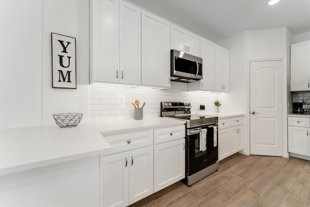 kitchen with light wood-type flooring, appliances with stainless steel finishes, light countertops, and white cabinets