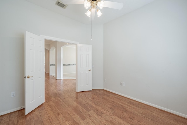 empty room with arched walkways, ceiling fan, visible vents, baseboards, and light wood finished floors