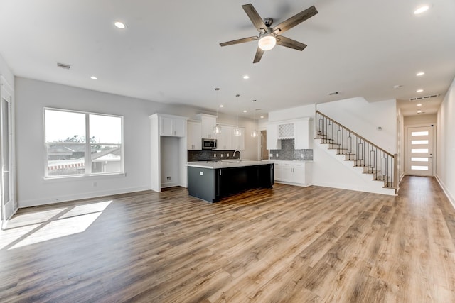 kitchen featuring visible vents, light wood-style floors, open floor plan, decorative backsplash, and stainless steel microwave