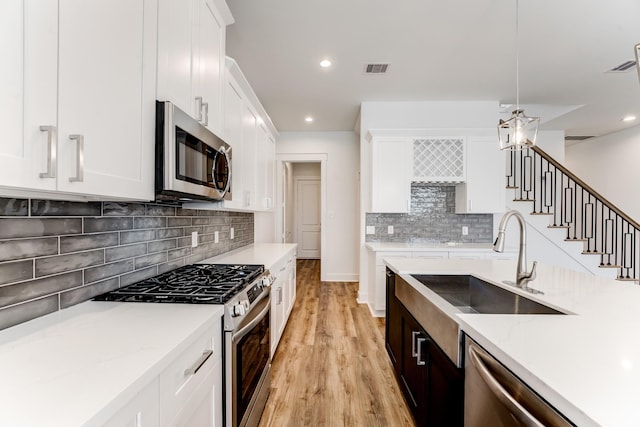 kitchen with stainless steel appliances, hanging light fixtures, light wood-style flooring, white cabinets, and a sink