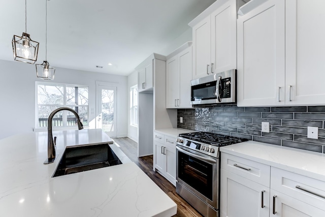 kitchen with appliances with stainless steel finishes, white cabinets, a sink, and decorative backsplash