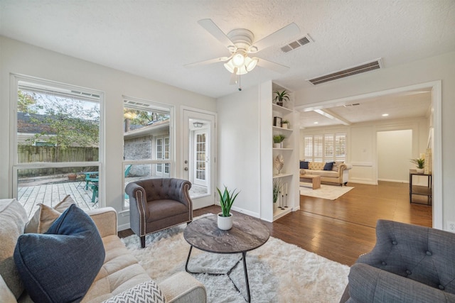 living area with visible vents, a textured ceiling, baseboards, and wood finished floors