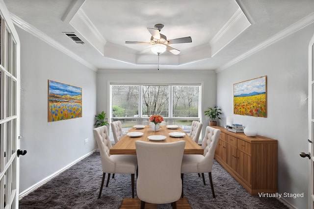 dining space with baseboards, a ceiling fan, ornamental molding, a tray ceiling, and dark colored carpet