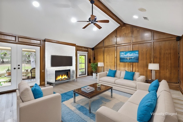 living area with wooden walls, a large fireplace, visible vents, light wood finished floors, and beamed ceiling