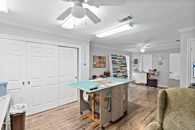 playroom with a textured ceiling, a ceiling fan, visible vents, light wood-style floors, and ornamental molding