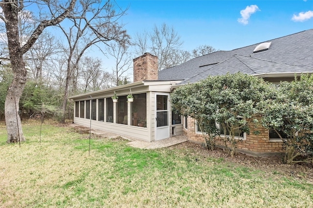 rear view of house with a yard, a shingled roof, a chimney, and a sunroom