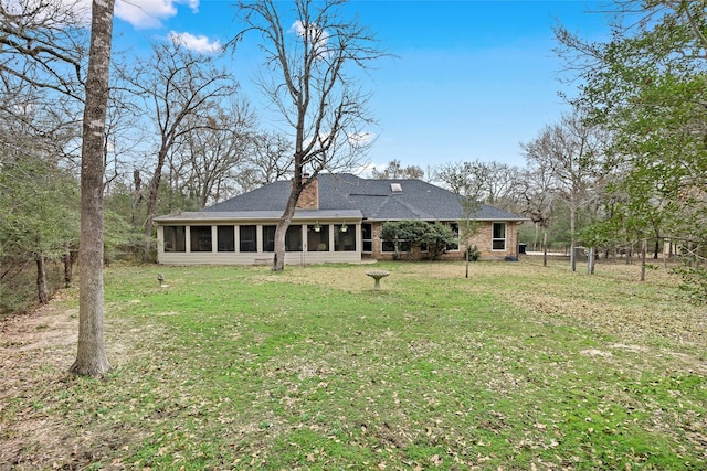 back of property featuring a sunroom, a shingled roof, a lawn, and brick siding