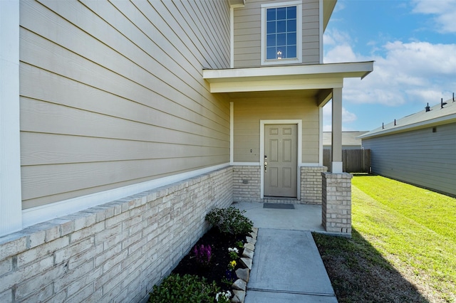 doorway to property featuring brick siding, a lawn, and fence