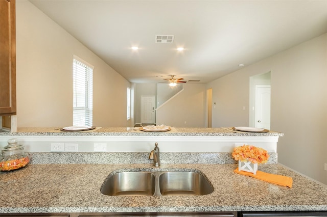 kitchen with light stone counters, visible vents, a sink, and a ceiling fan