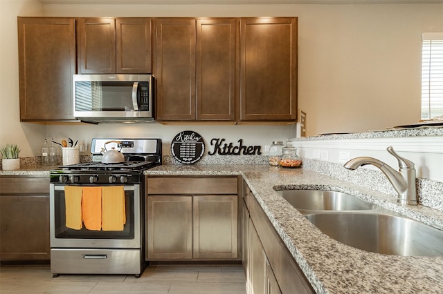 kitchen featuring light stone countertops, stainless steel appliances, and a sink