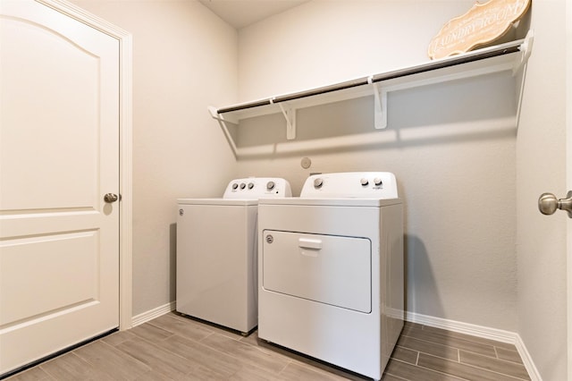 laundry room featuring laundry area, washing machine and dryer, baseboards, and wood finish floors