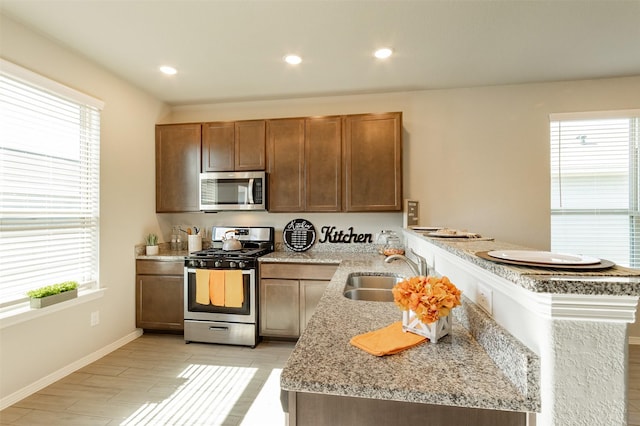 kitchen featuring recessed lighting, stainless steel appliances, a peninsula, a sink, and baseboards