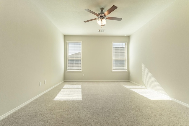 carpeted spare room featuring a ceiling fan, visible vents, plenty of natural light, and baseboards