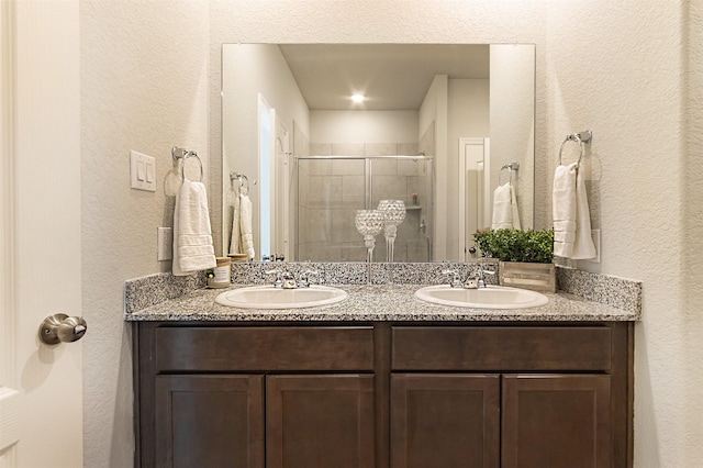 full bathroom with double vanity, a shower stall, a sink, and a textured wall