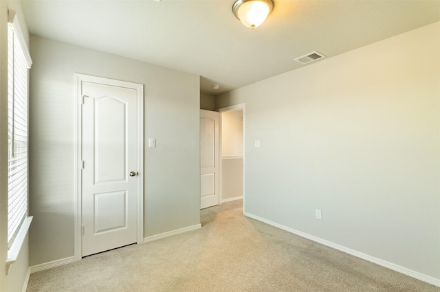 unfurnished bedroom featuring light carpet, multiple windows, visible vents, and baseboards