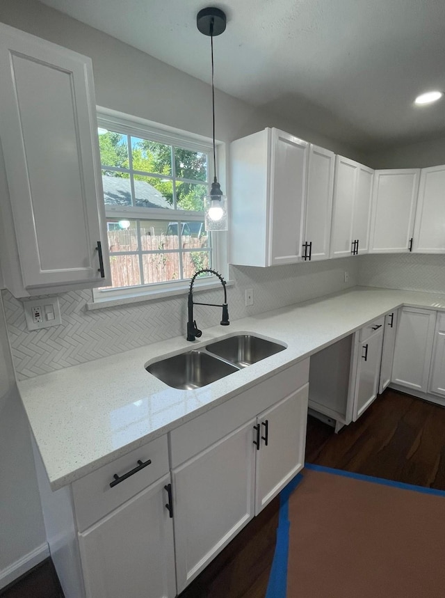 kitchen with dark wood-type flooring, hanging light fixtures, a sink, white cabinetry, and backsplash