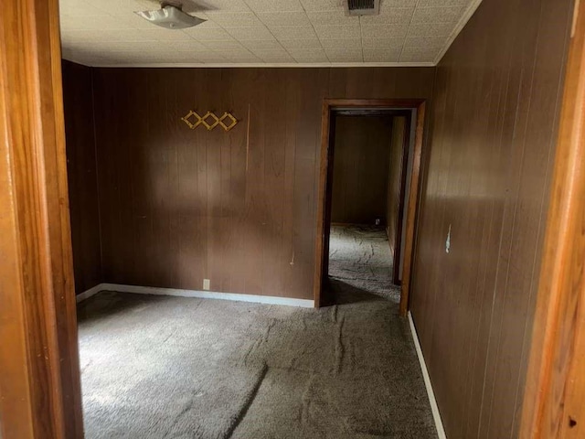 carpeted empty room featuring ornamental molding, visible vents, wood walls, and baseboards