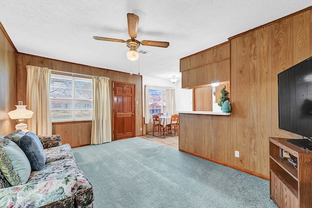 living area with wood walls, visible vents, a textured ceiling, and light colored carpet