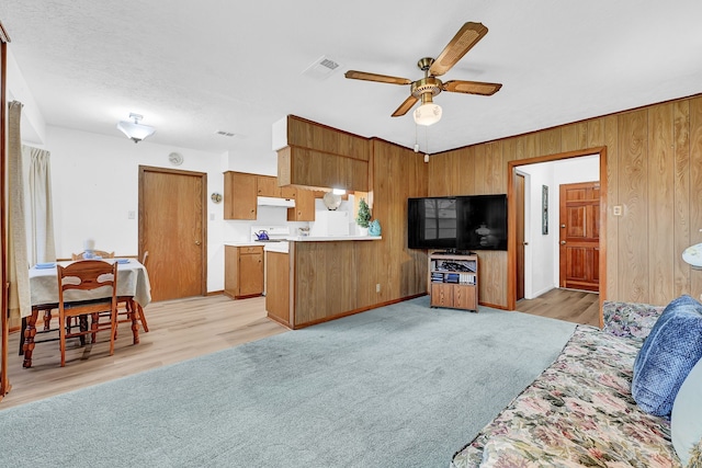 living area with ceiling fan, wooden walls, visible vents, and light colored carpet