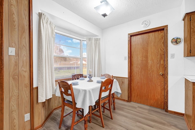 dining space with light wood-style floors, wainscoting, wood walls, and a textured ceiling